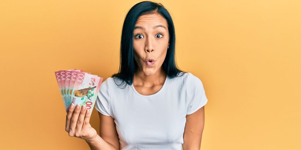 Surprised Kiwi woman holding NZ money, learning 6 tips to improve bad credit loan approval chances with East Bay Finance.